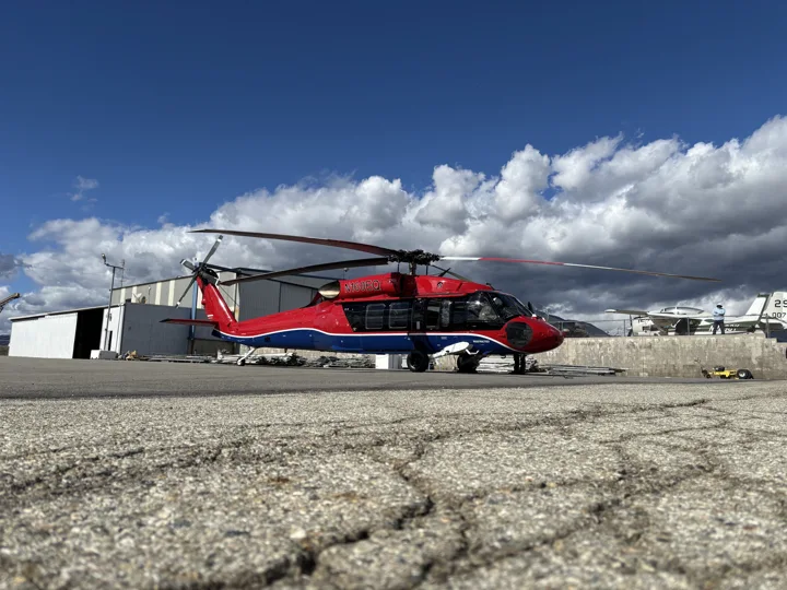 Full side view of a red, black and blue helicopter outside the hangar